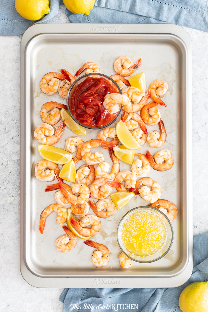 Overhead of Roasted Shrimp Cocktail with melted butter, cocktail sauce and shrimp and lemon wedges on pan