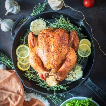 A whole smoked chicken in a cast iron skillet garnished with lime and fresh herbs.