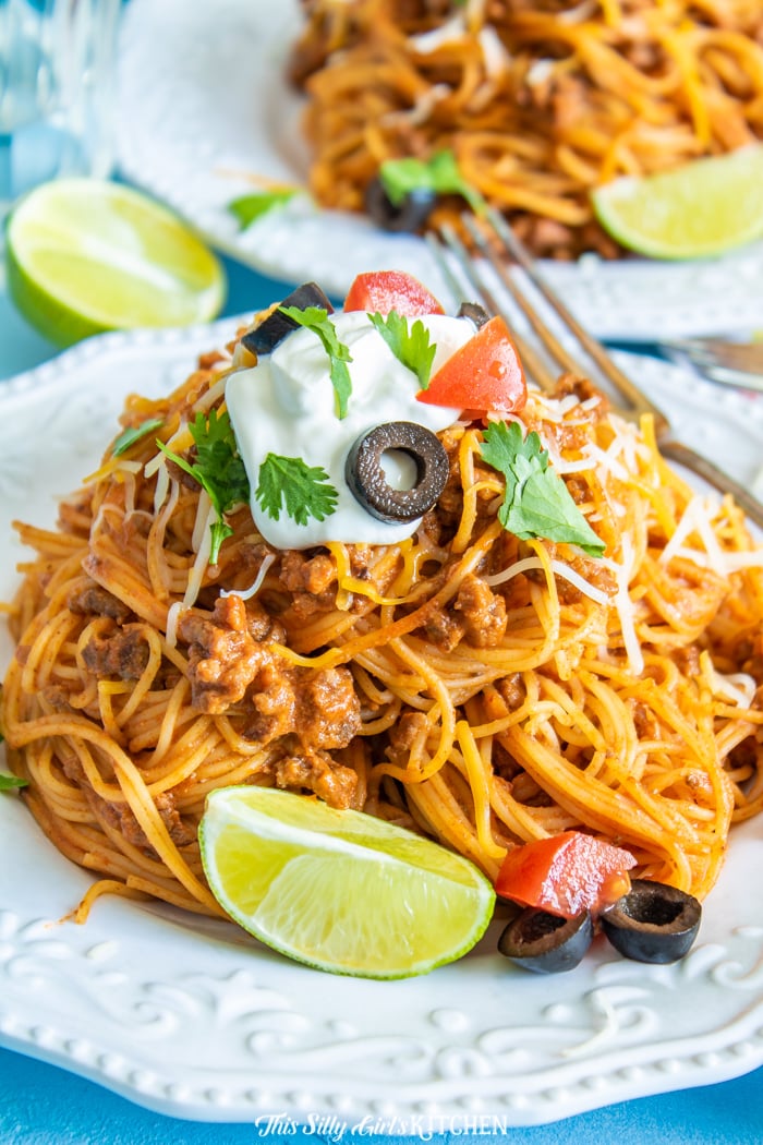 Taco Pasta on white plate topped with sour cream, olives and tomatoes
