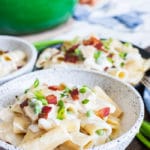 A bowl of creamy Ranch Chicken Pasta topped with crispy bacon and scallions with a green dutch oven behind it.