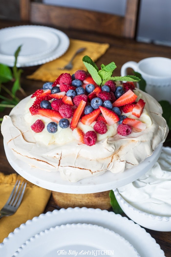 Pavlova topped with pastry cream, berries and mint on cake stand