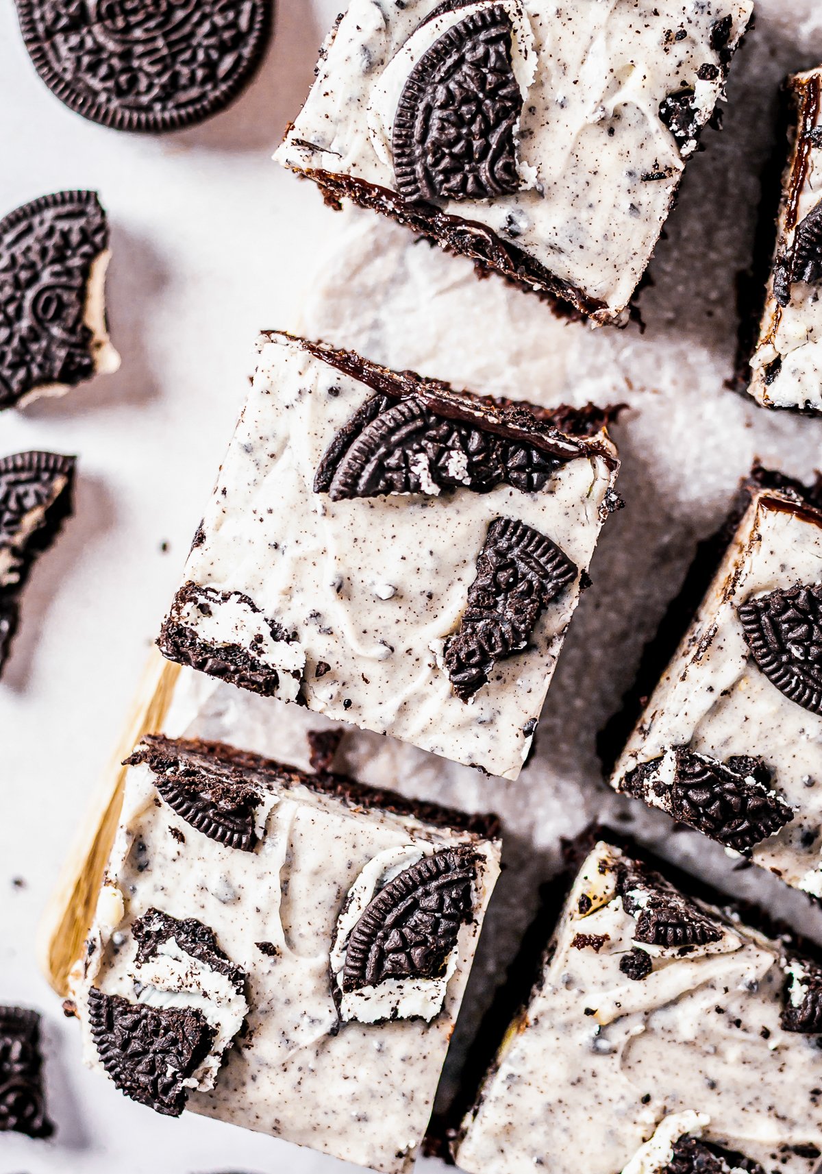 Overhead of cut brownies on wooden board showing Oreos on top.