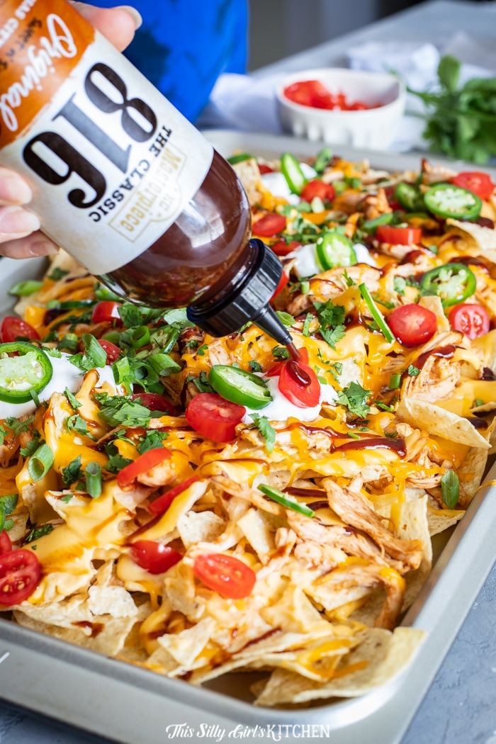 BBQ Sauce being drizzled over Nachos on pan
