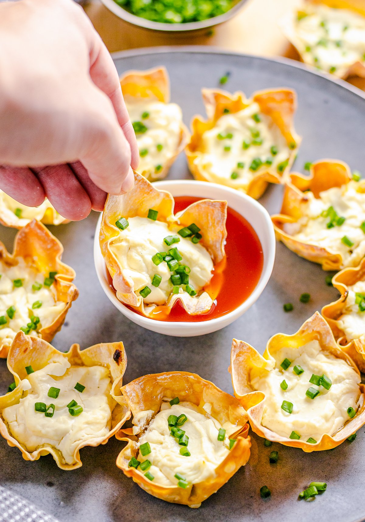 Hand dipping one Baked Cream Cheese Wonton Cup in dipping sauce.