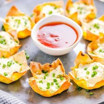 Square image of wontons on plate with dipping sauce in middle.