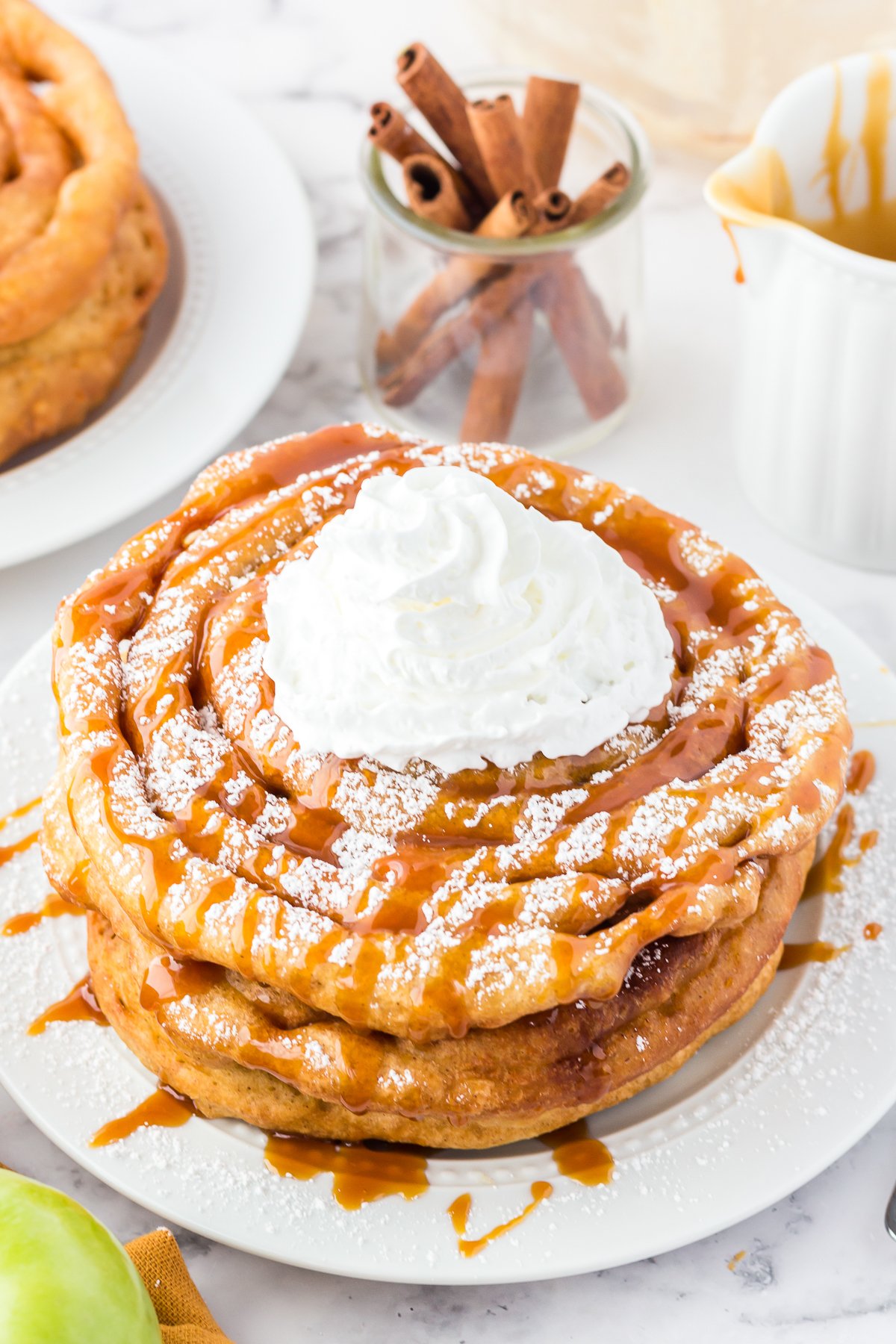 Stack of Caramel Apple Funnel Cakes topped with powdered sugar, caramel sauce and whipped topping.