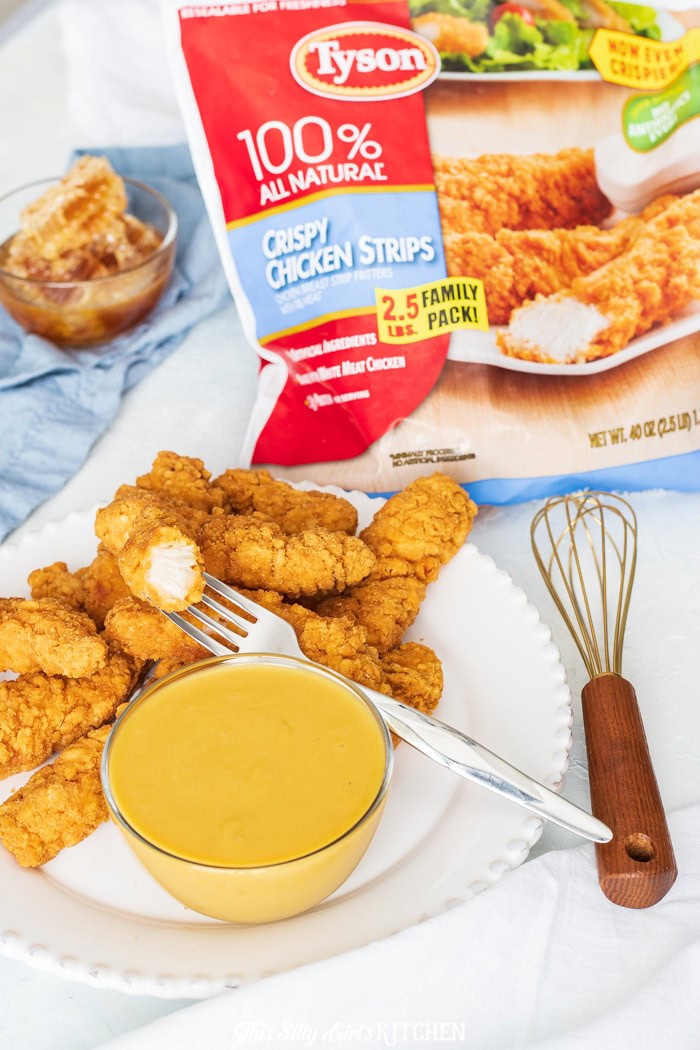 Homemade Honey Mustard sauce in a bowl with a whisk and crispy chicken tenders.