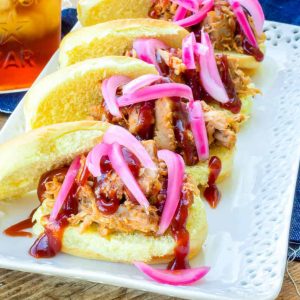 Close up of Pulled Pork Sliders topped with BBQ sauce and pickled red onions on a white platter.