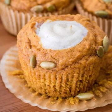 A pumpkin muffin with a cream cheese center and pumpkin seeds on a plate.