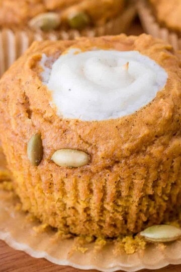 A pumpkin muffin with a cream cheese center and pumpkin seeds on a plate.