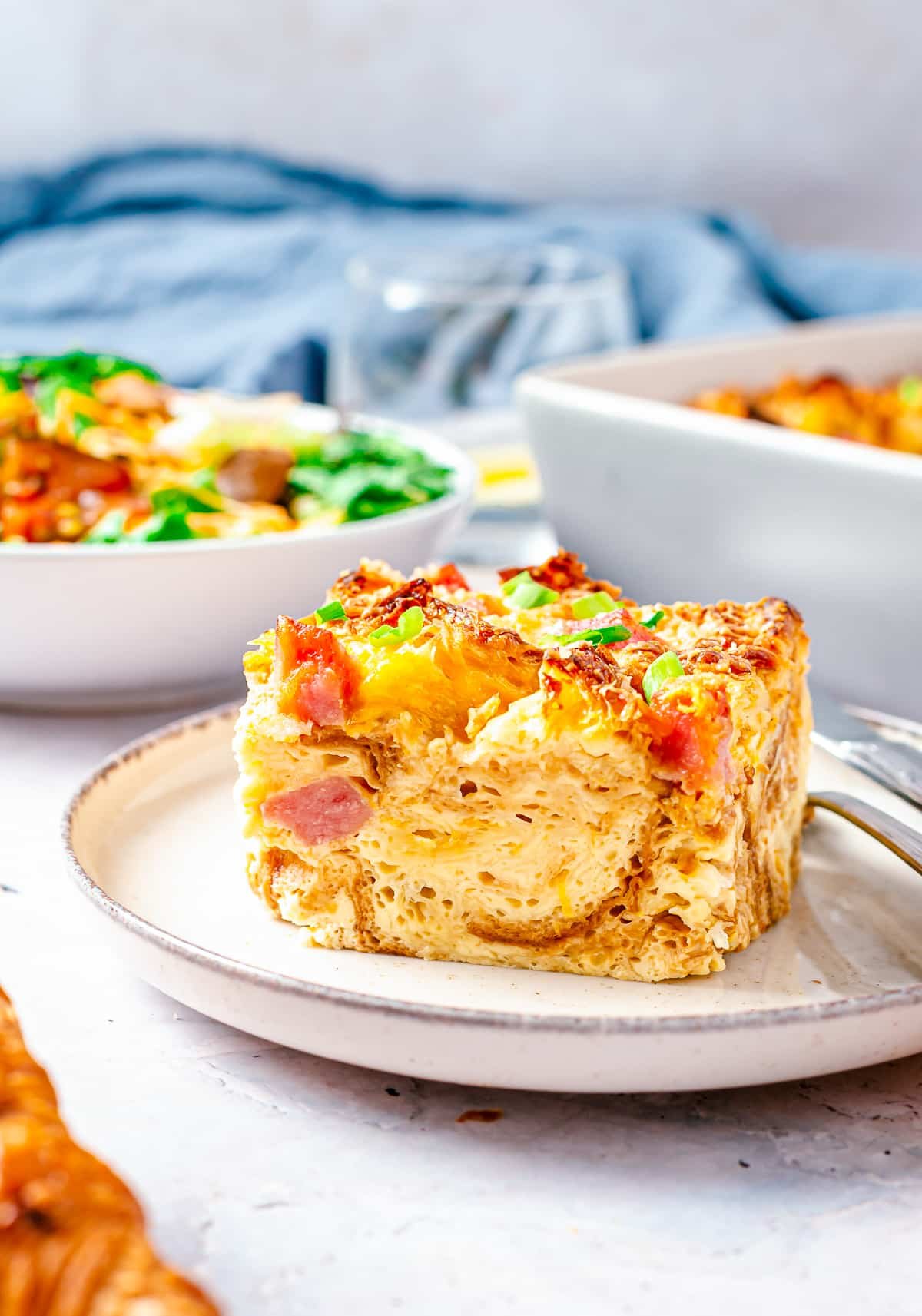 Close up side view of slice of Ham and Cheese Savory Bread Pudding showing layers on white plate.