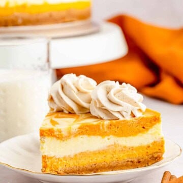 One slice of the Pumpkin Cheesecake on white plate with whole cheesecake on stand in background.