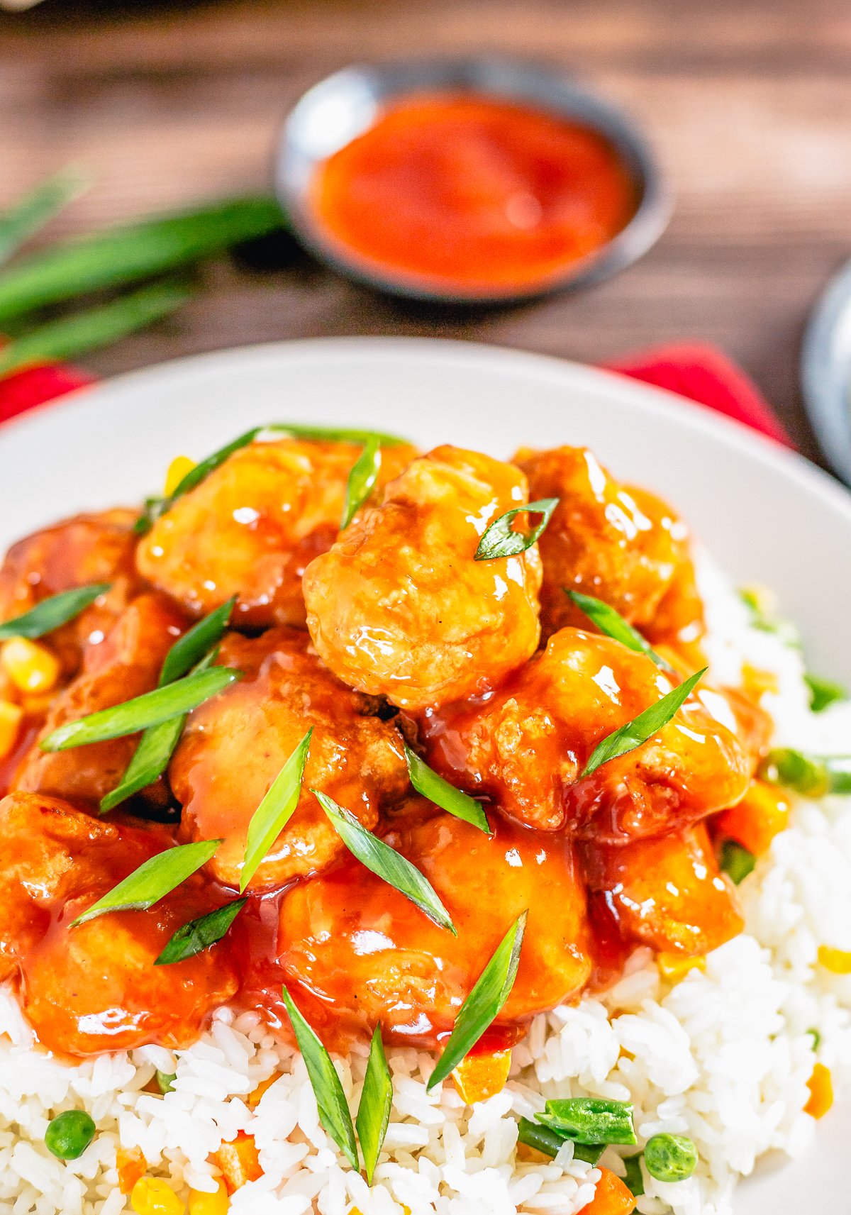 Close up of The Best Sweet and Sour Chicken over rice with garnishes.