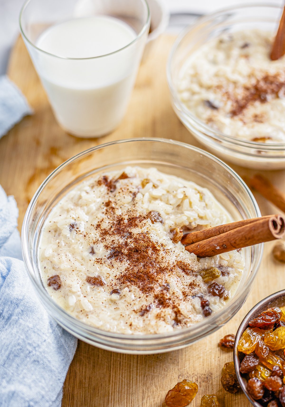 Bowl of Rice Pudding Recipe with cinnamon and golden raisins on side.