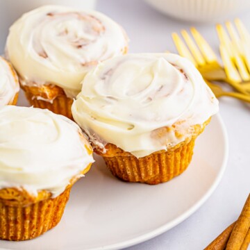 Close up of three Cinnamon Roll Buns on plate with coffee in background.