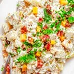 A platter of Ranch Potato Salad topped with crispy bacon, cheddar cubes, fresh dill, and scallions.