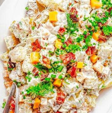 A platter of Ranch Potato Salad topped with crispy bacon, cheddar cubes, fresh dill, and scallions.