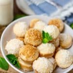 A white bowl piled with baked donut holes topped with toasted and shredded coconut over vanilla glaze.