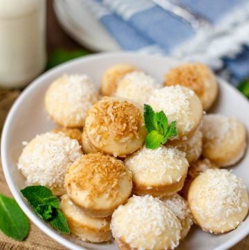 A white bowl piled with baked donut holes topped with toasted and shredded coconut over vanilla glaze.