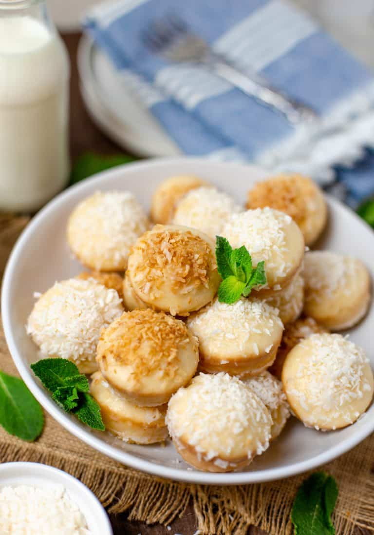 A white bowl piled with baked donut holes topped with toasted and shredded coconut over vanilla glaze.