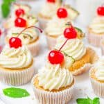 Pina colada cupcakes topped with frosting, toasted coconut, and cherries.