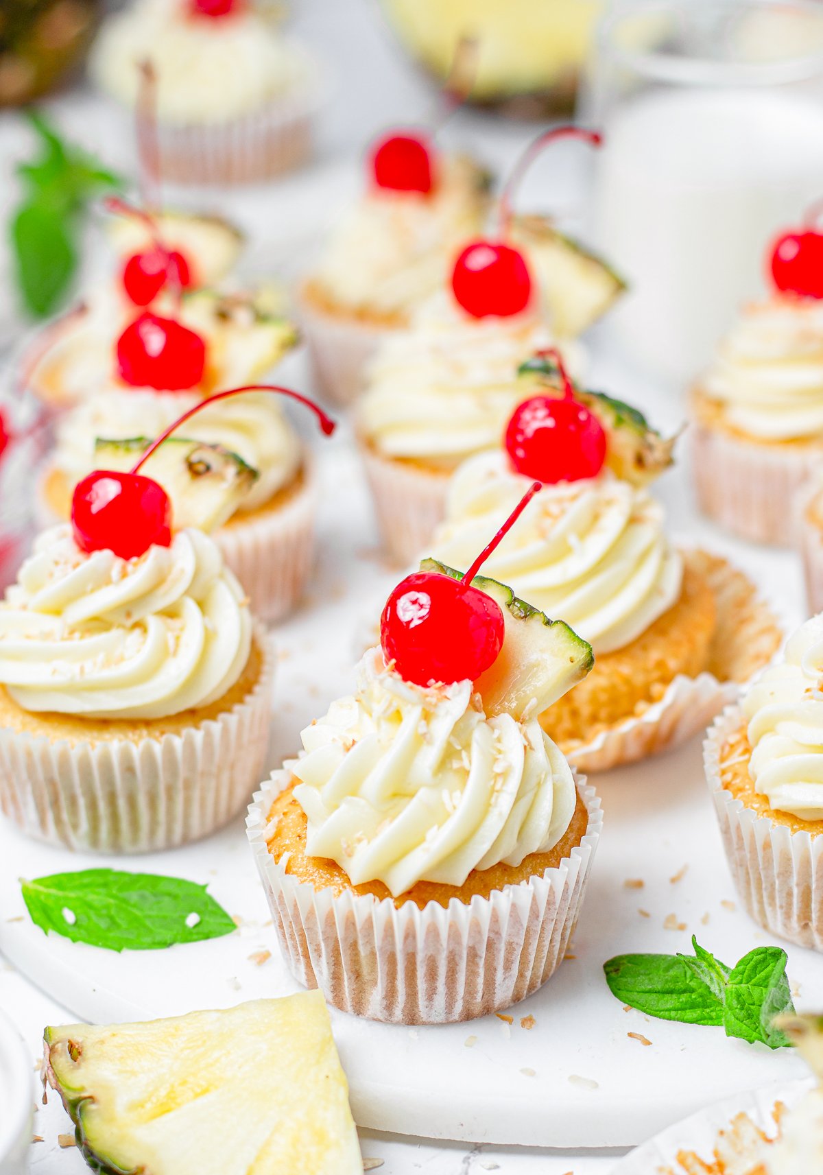 Pina Colada Cupcakes decorated topped with cherries on white platter