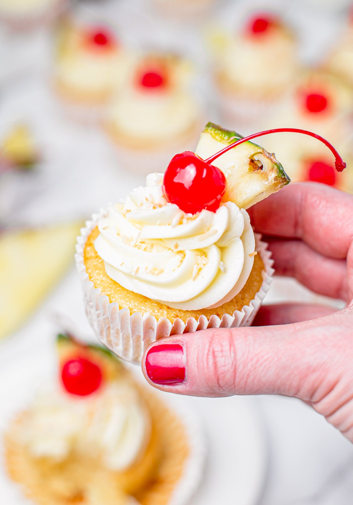 Hand holding one Pina Colada Cupcake showing frosting and toppings