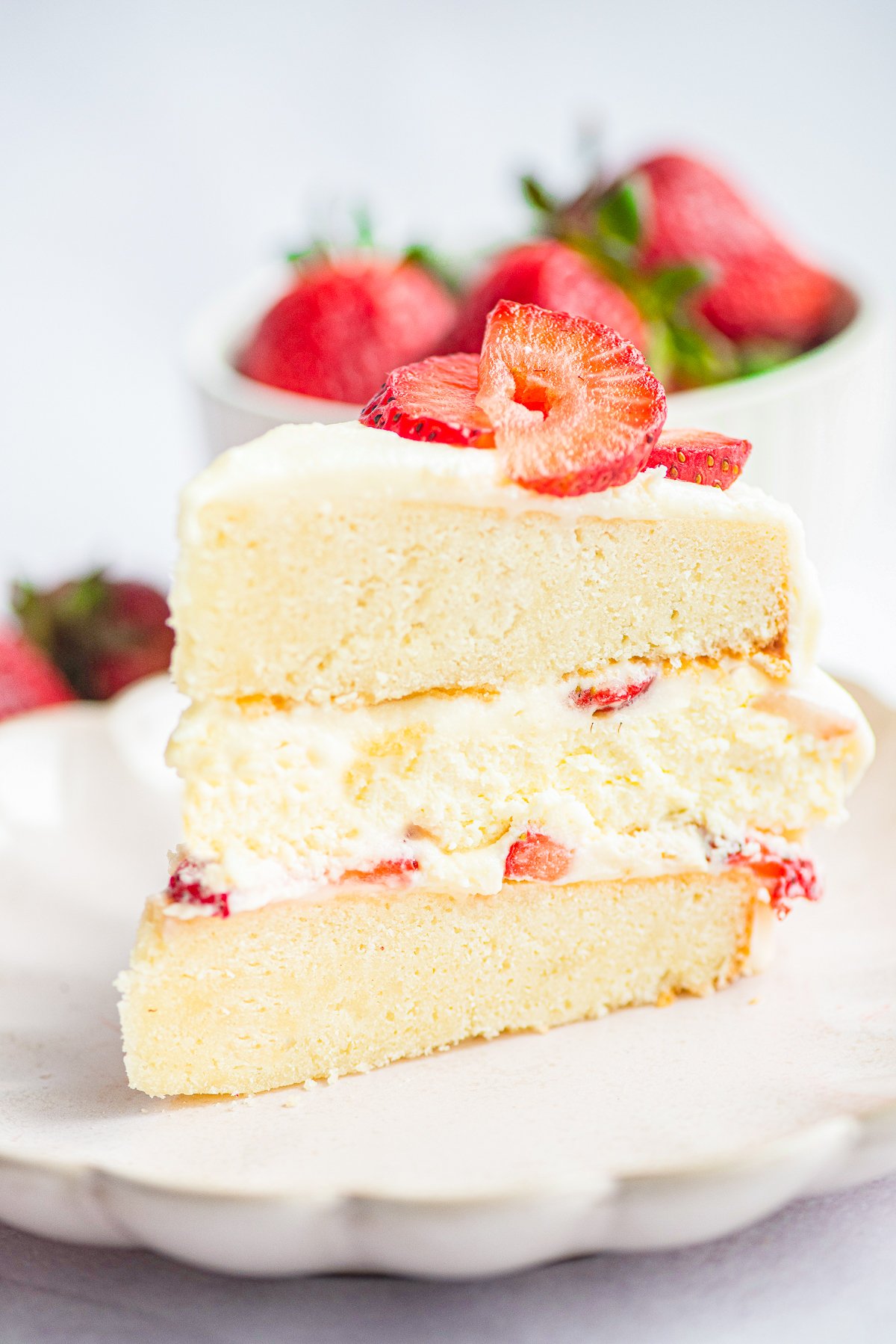 Slice of cake on white plate showing each layers topped with strawberries