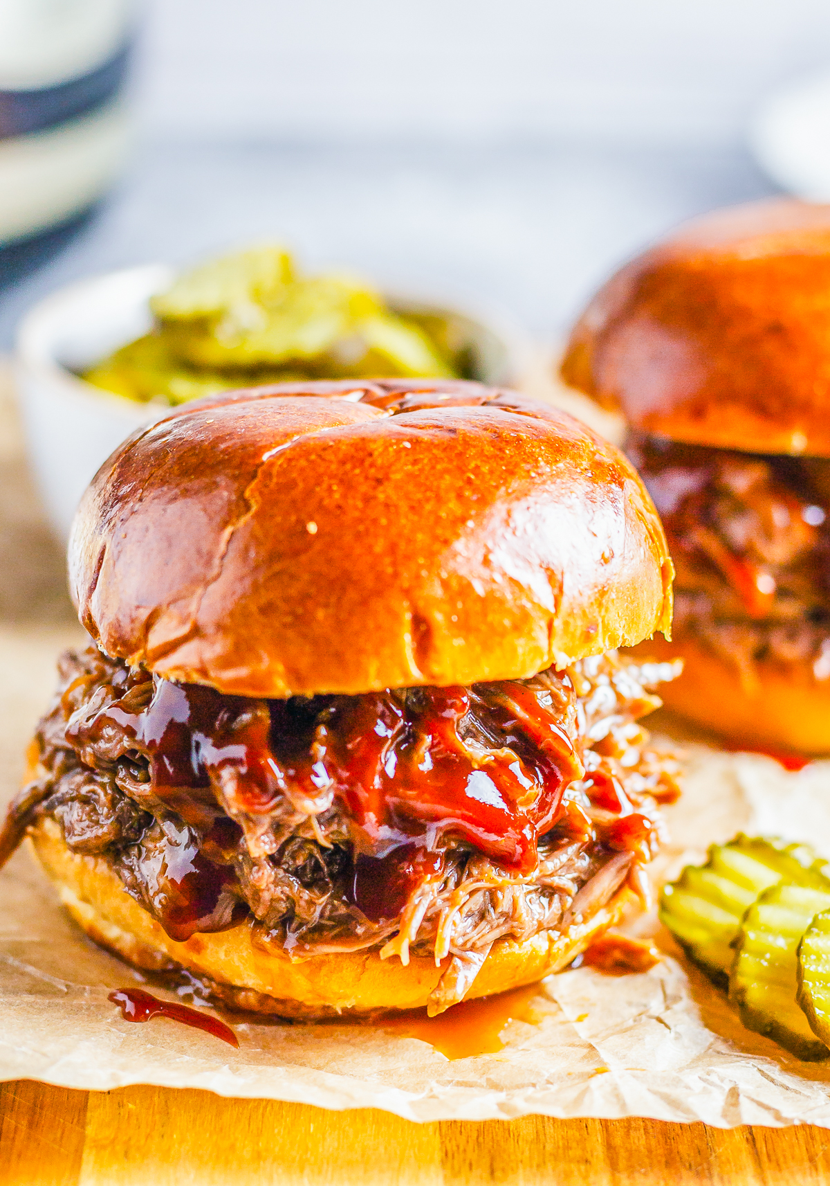 Slow Cooker BBQ Beef Sandwiches on parchment with dripping bbq sauce and pickles laying by sandwich.
