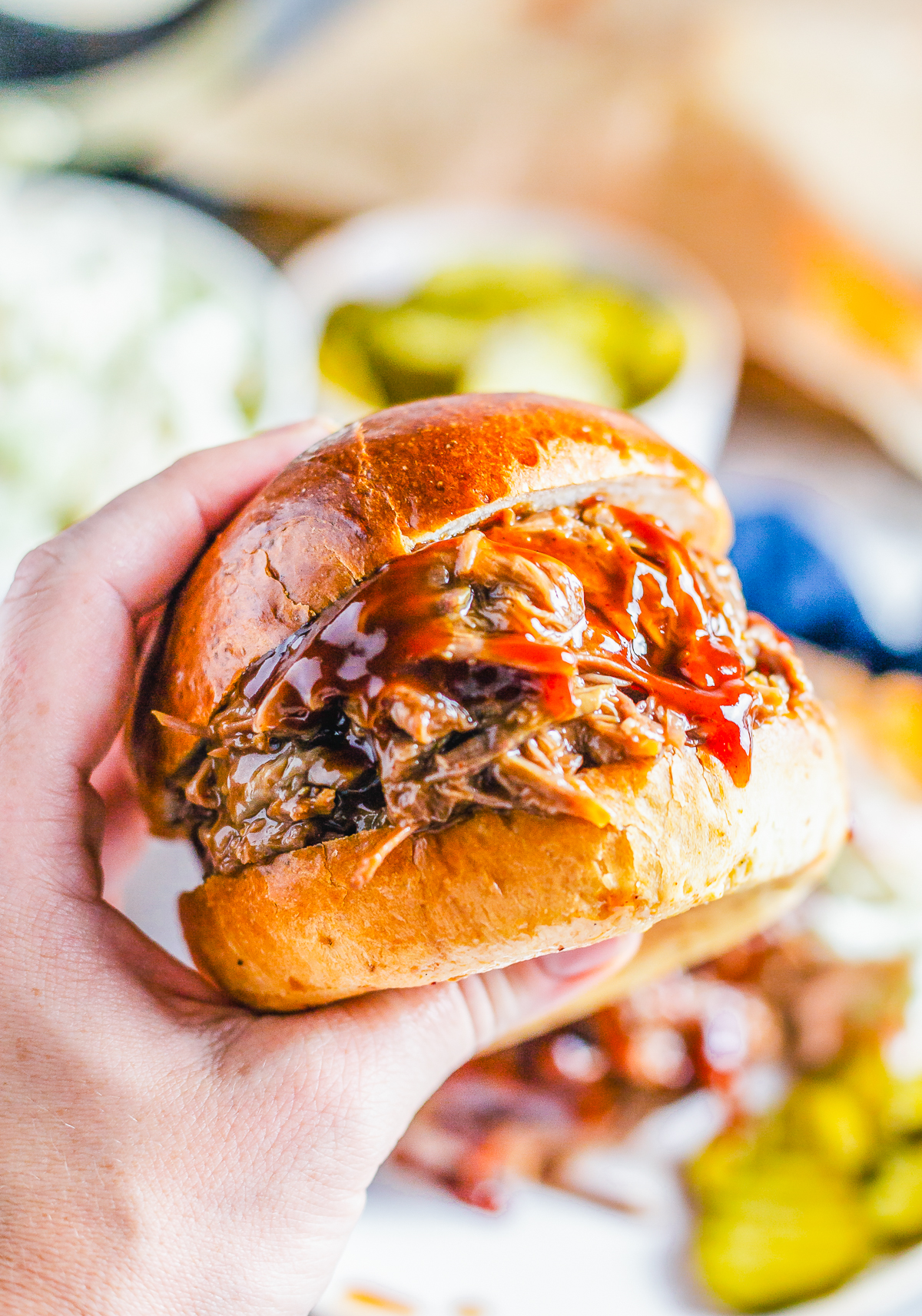 BBQ Beef Sandwich being held in hand showing meat and BBQ saucce.