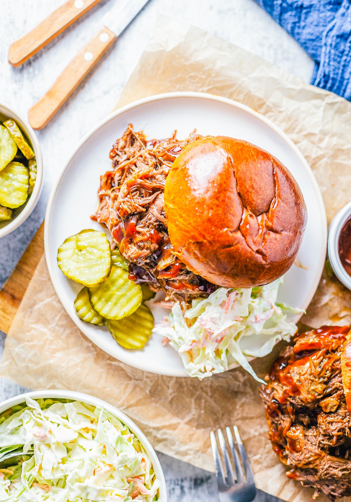 Overhead of plated Slow Cooker BBQ Beef Sandwiches with pickles and coleslaw.