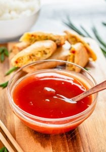 Spoon lifting glossy Sweet and Sour Sauce from a white bowl.