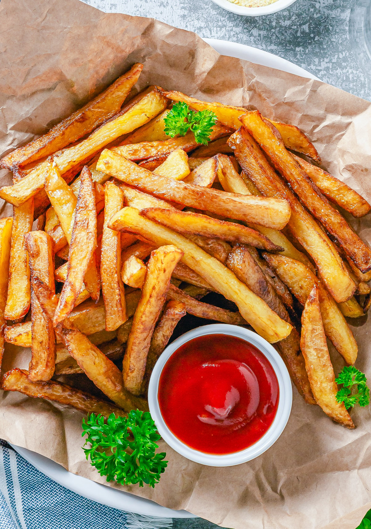 Overhead photo of French Fries on parchment paper with ketchup and parsley.
