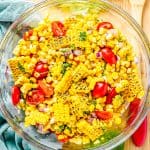 A glass bowl of fresh corn and tomato salad with basil and red onion.