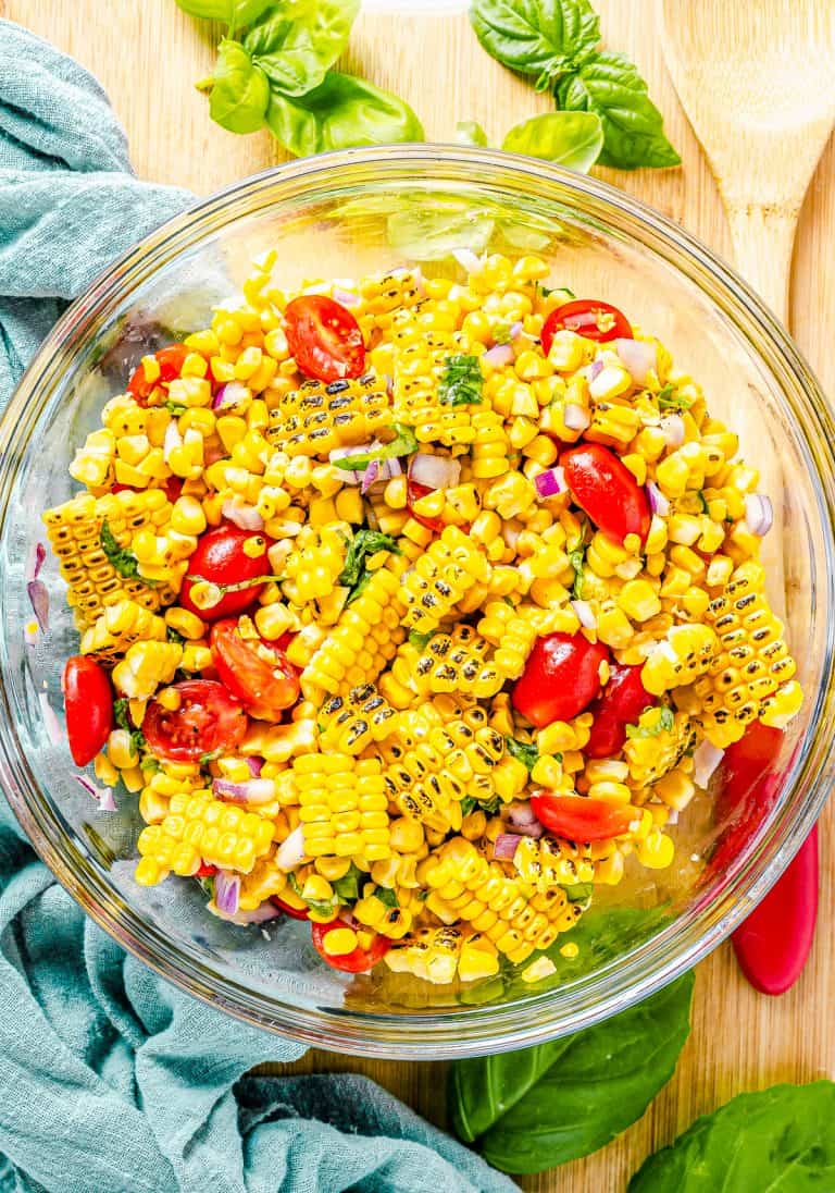 A glass bowl of fresh corn and tomato salad with basil and red onion.