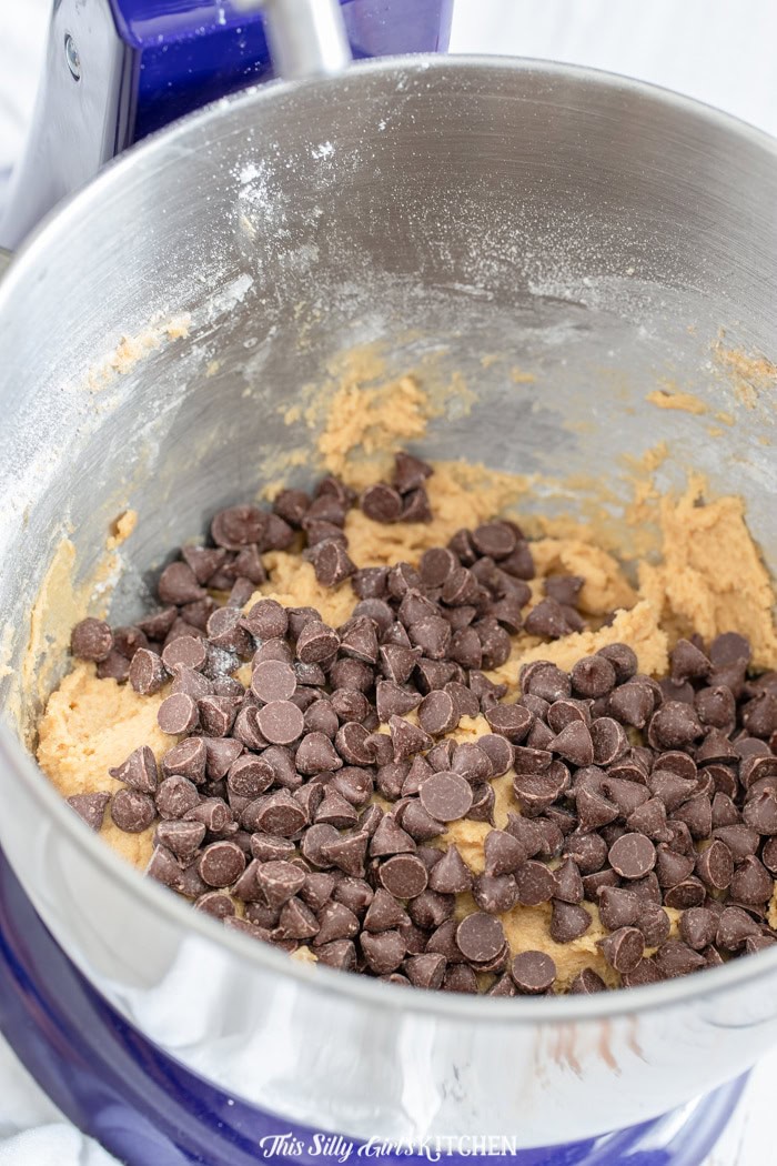 Chocolate chips being folded into chocolate chip cookie dough in a mixing bowl.