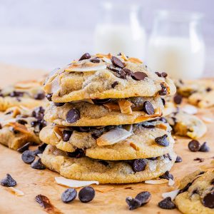 Stacked cookies on parchment paper with chocolate chips and coconut around them.