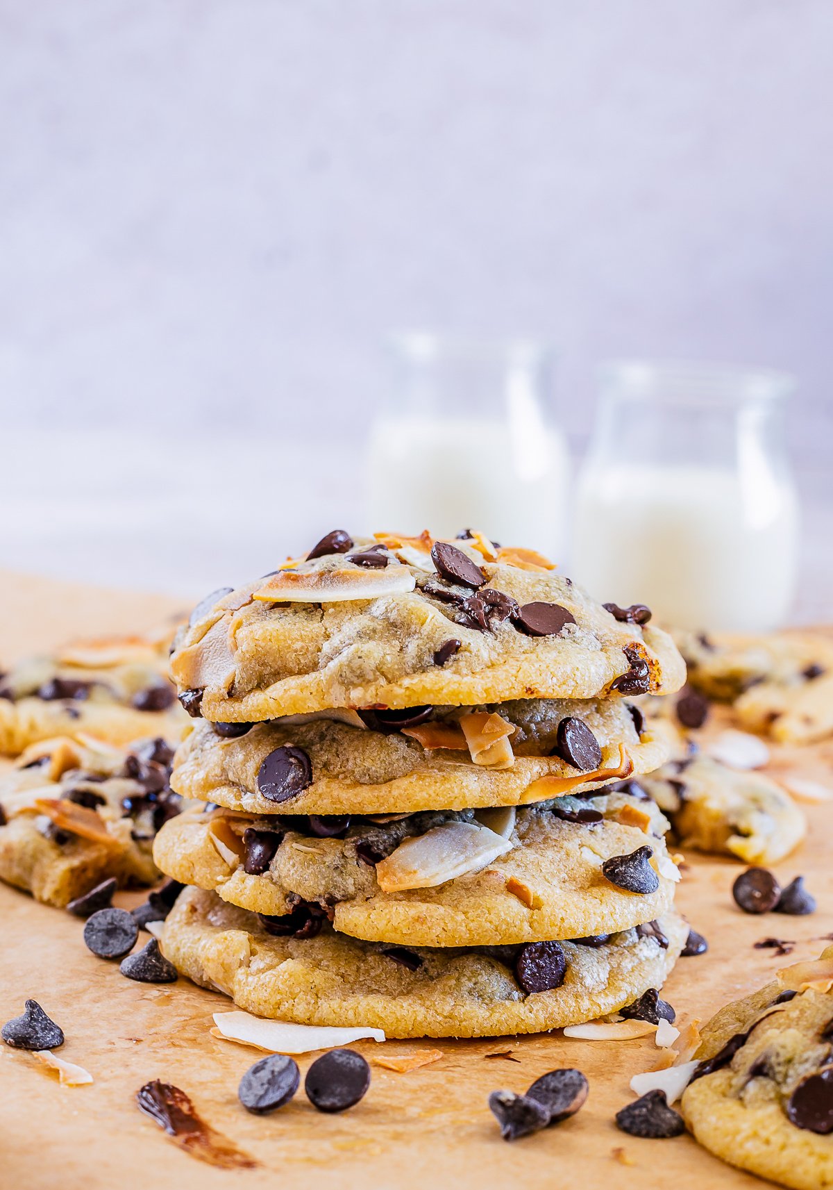 Four Coconut Chocolate Chip Cookies stacked on top of one another with milk in backgound.