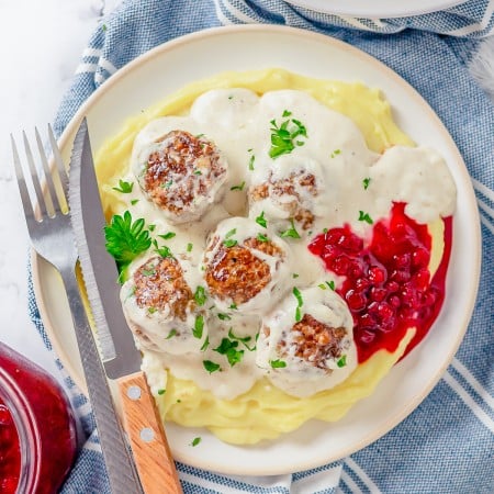 Square image overhead of plated meatballs on plate with mashed potatoes.