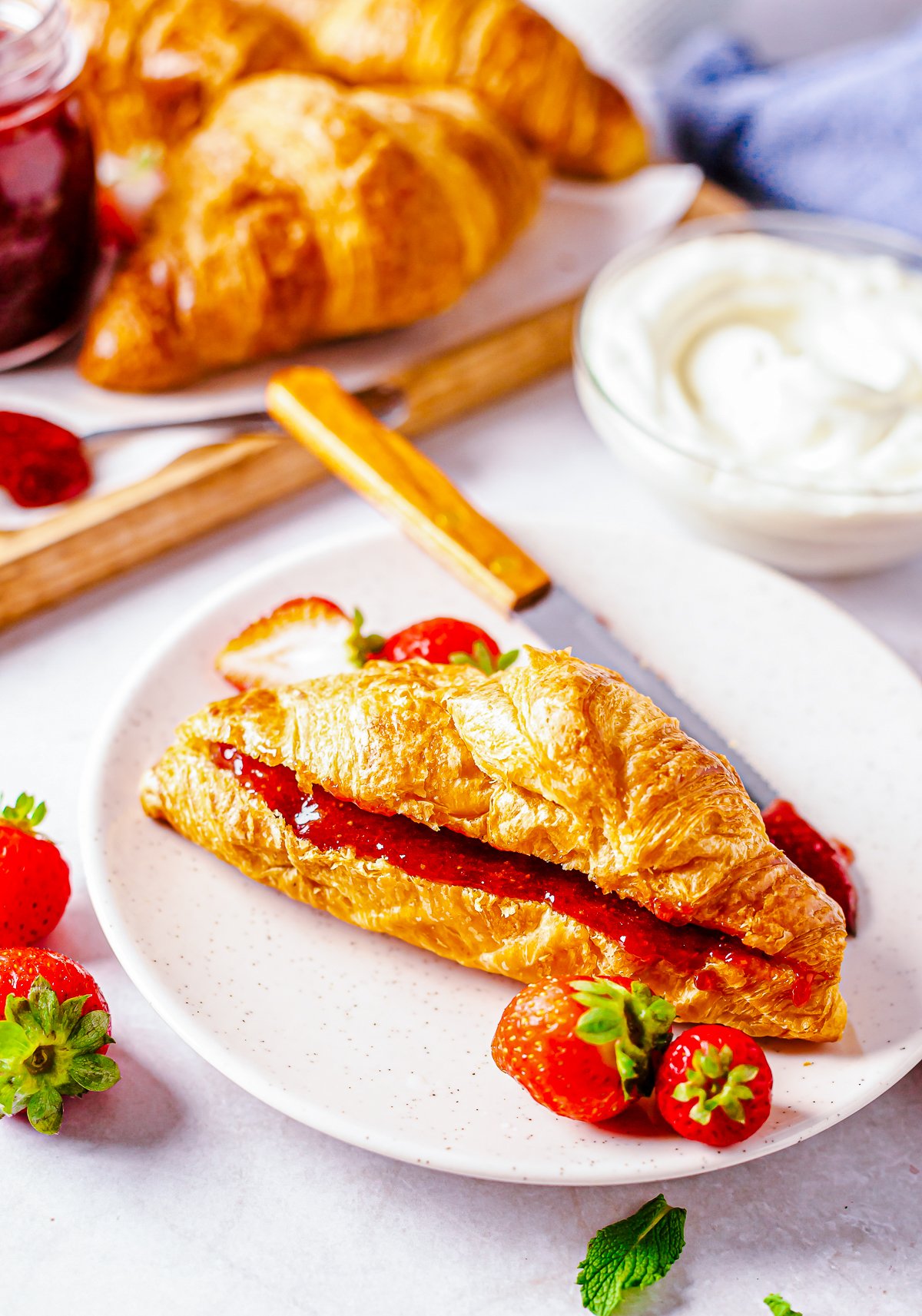 One Croissant spread with Strawberry Butter on plate with strawberries.