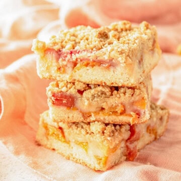 A stack of peach bars with crumble topping on a white surface.