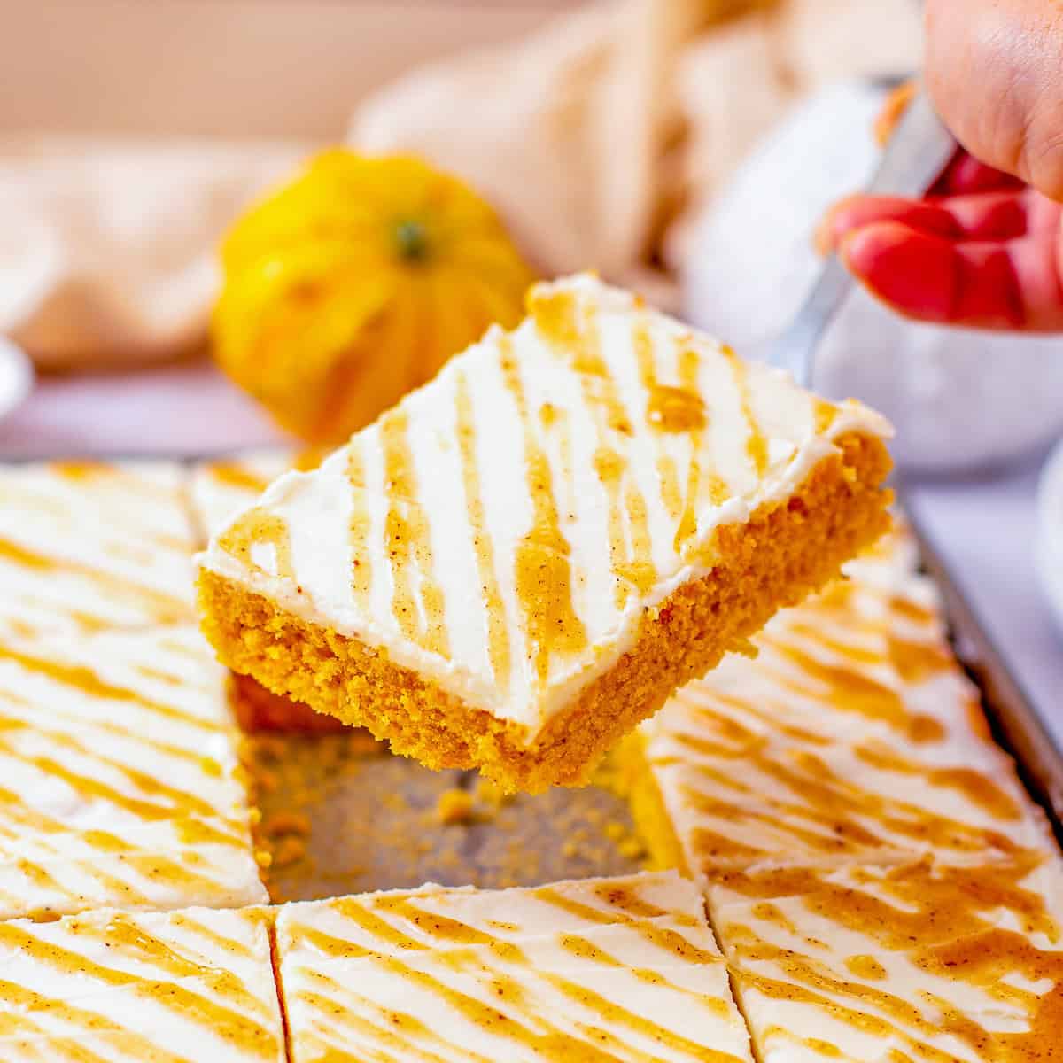 Squares of caramel pumpkin sheet cake stacked and drizzled with pumpkin spice caramel sauce.