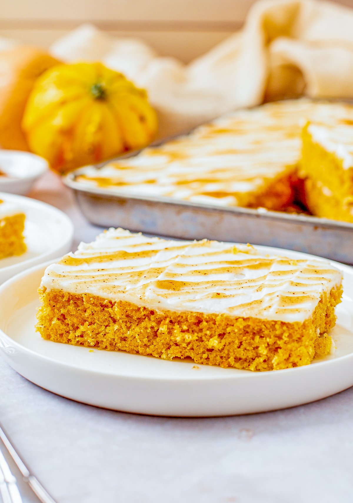 Slice of Pumpkin Sheet cake on white plate with pan of cake in background.