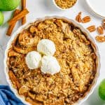 A baked apple crumble in a white dish topped with a scoop of vanilla ice cream.