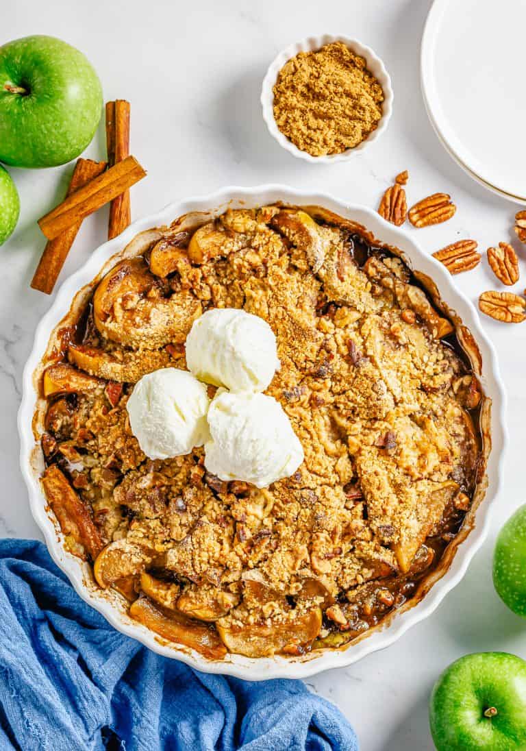 A baked apple crumble in a white dish topped with a scoop of vanilla ice cream.