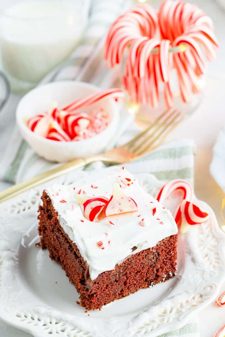 A slice of chocolate peppermint poke cake on a white plate with candy canes.