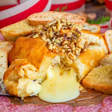 Baked brie in puff pastry topped with honey walnuts on a charcuterie board.