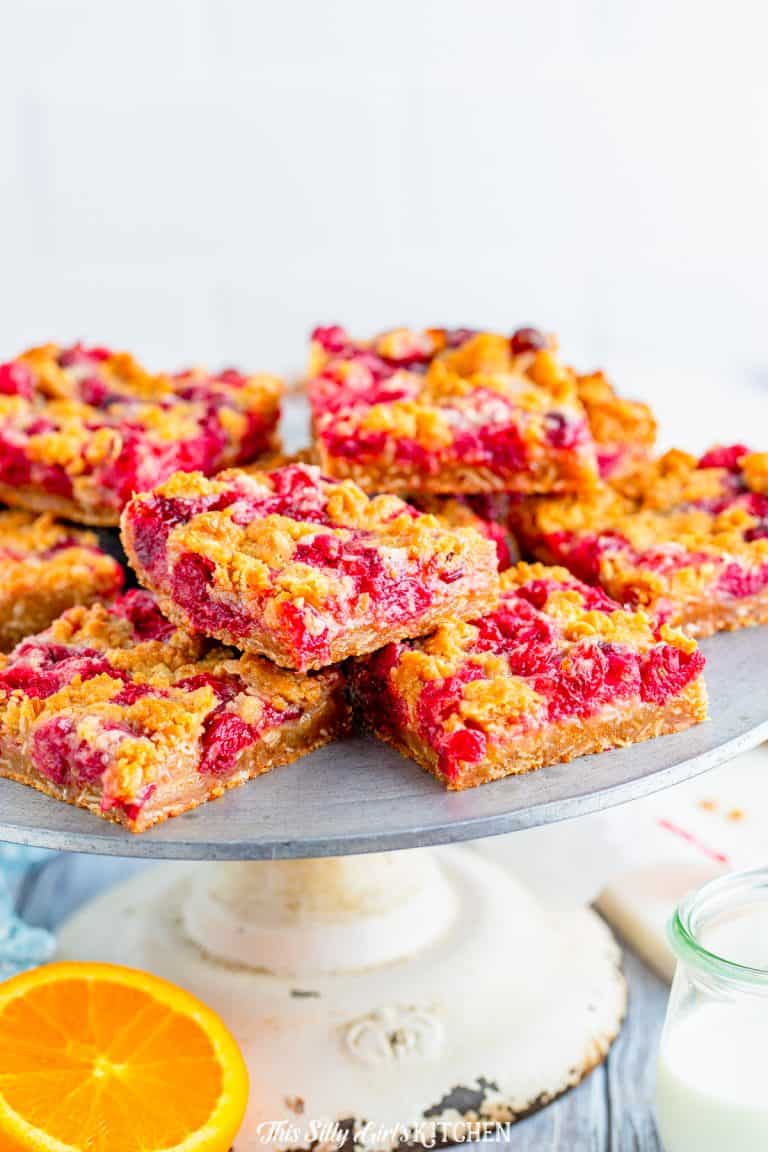 A stack of cranberry bars on a cake stand showing the ruby red cranberry filling between golden oat crumble layers.
