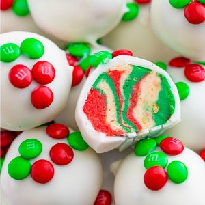 Oreo Balls dipped in white almond bark and topped with mini M and Ms, one cut open to show the red and green swirled center.