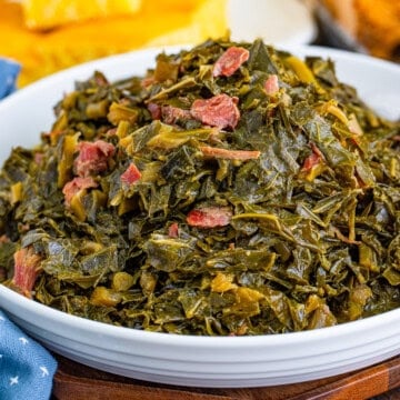 Bowl of Southern Collard Greens Recipe with shredded ham hocks served alongside cornbread and fried chicken.